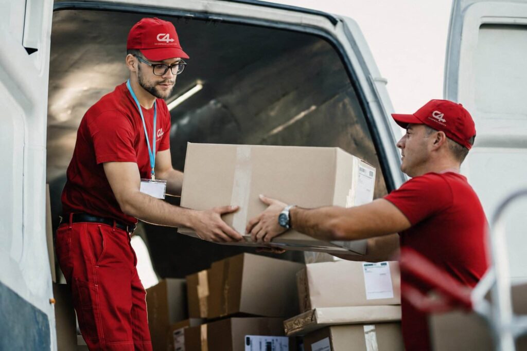 Two couriers loading a cardboard box into a delivery van